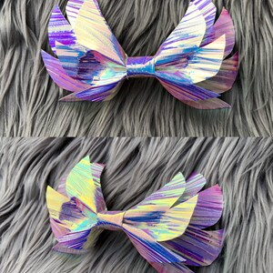 May include: A large iridescent bow with a layered, wing-like design. The bow is made of a shiny, holographic material with shades of purple, blue, and gold.