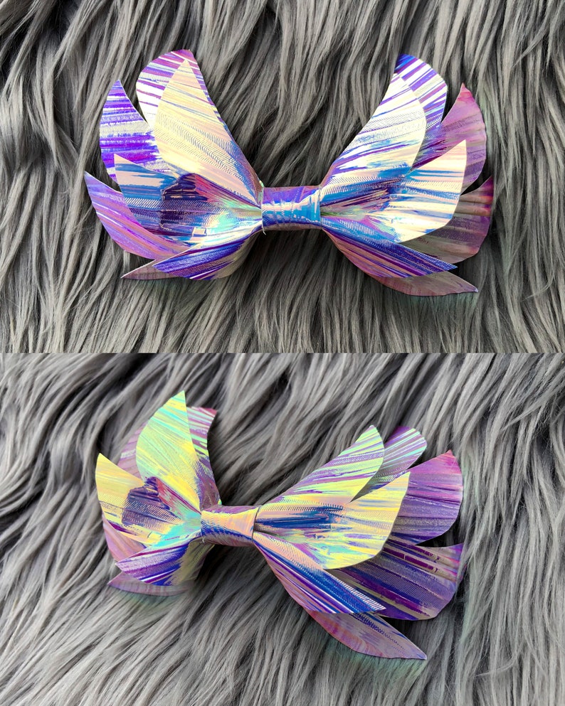 May include: A large iridescent bow with a layered, wing-like design. The bow is made of a shiny, holographic material with shades of purple, blue, and gold.