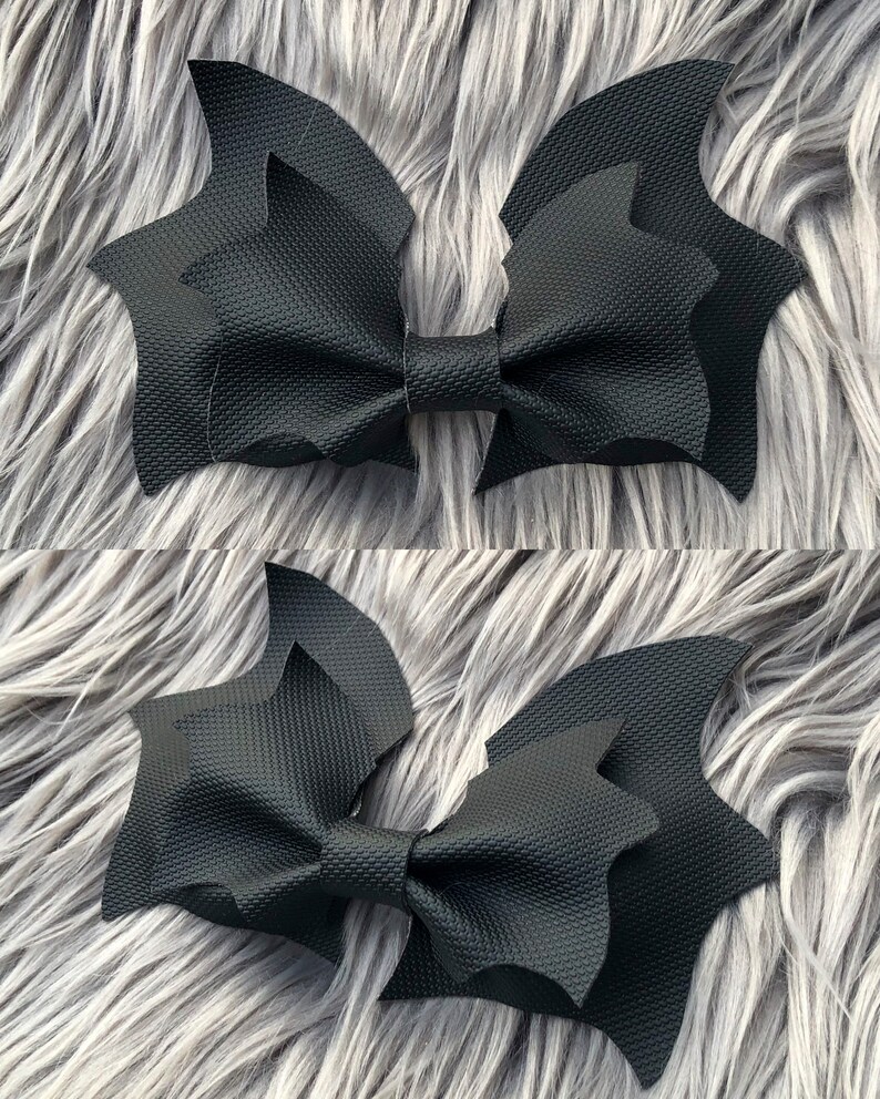 K&ouml;nnte beinhalten: Zwei schwarze Fledermaus-Haarspangen mit strukturierter Oberfl&auml;che. Die Schleifen sind &uuml;bereinander gelegt und in der Mitte gebunden.