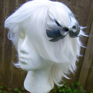 May include: A silver glitter bow with wings, worn in a white wig.