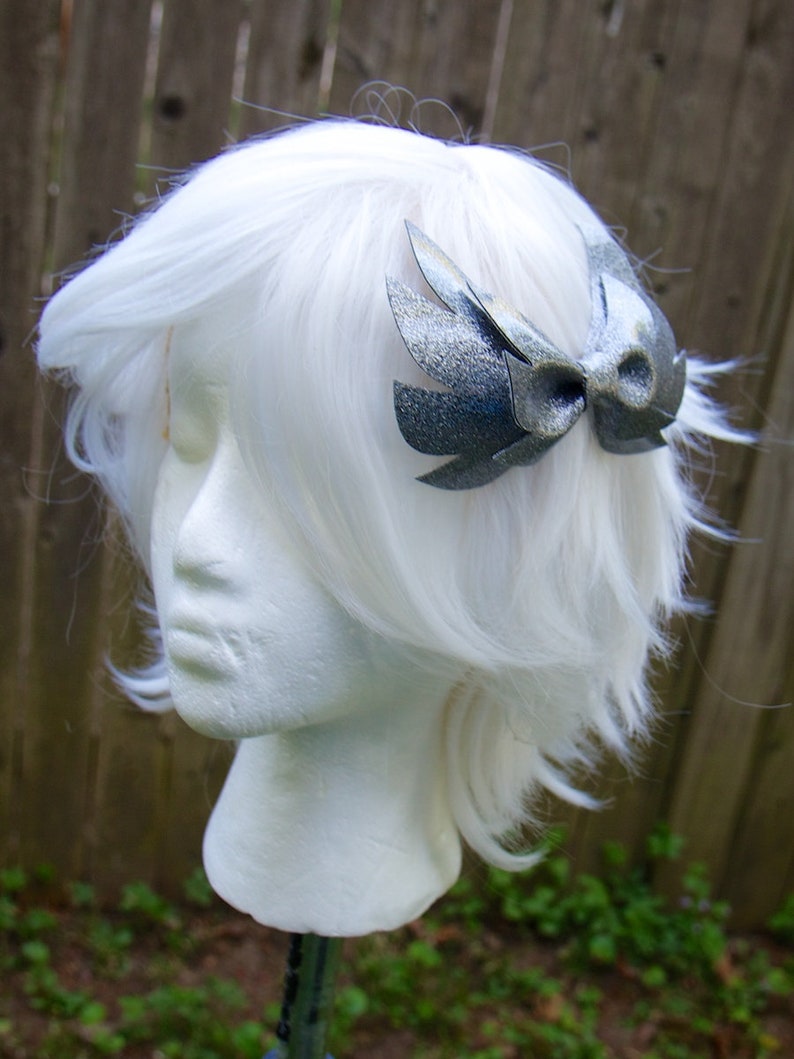 May include: A silver glitter bow with wings, worn in a white wig.