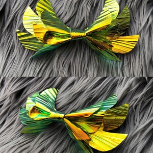 May include: A large, gold and green iridescent bow with a layered, pleated design. The bow is made of a shiny, metallic material.