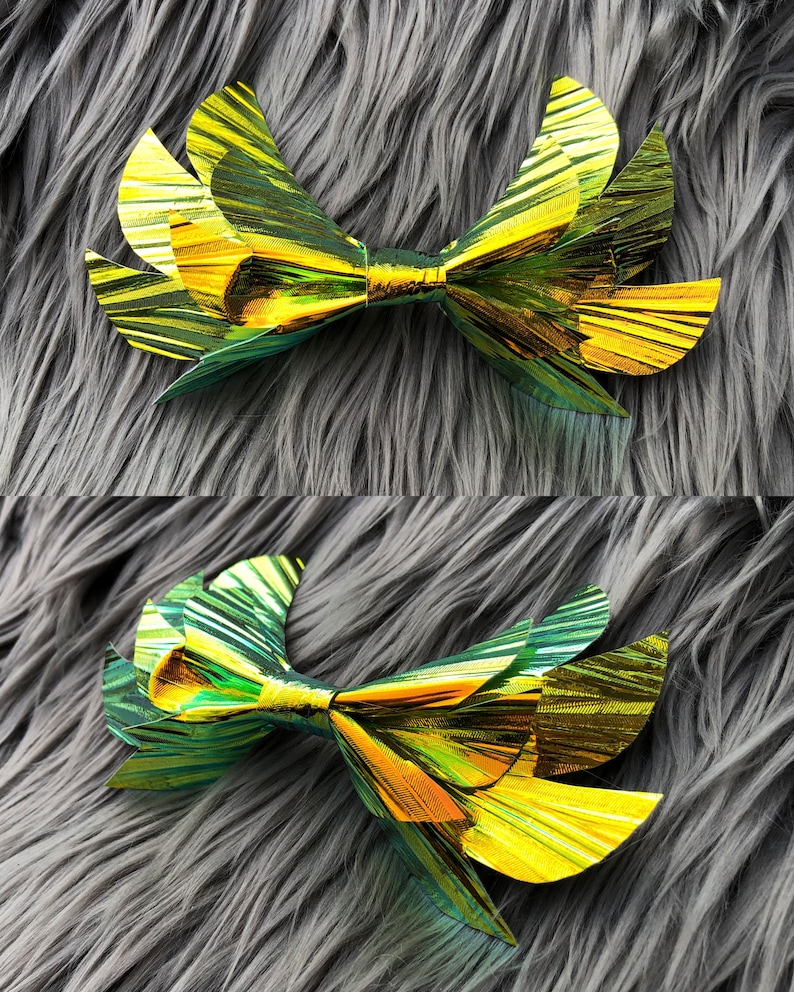 May include: A large, gold and green iridescent bow with a layered, pleated design. The bow is made of a shiny, metallic material.