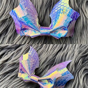 K&ouml;nnte beinhalten: Eine gro&szlig;e, regenbogenfarbene Schleife in Lila und Blau mit der Form von Fledermausfl&uuml;geln. Die Schleife besteht aus einem Material mit sechseckigem Muster.