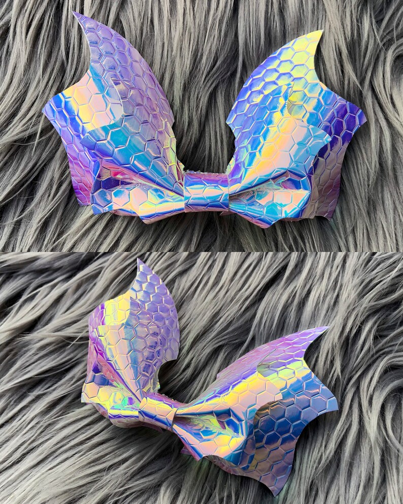 K&ouml;nnte beinhalten: Eine gro&szlig;e, regenbogenfarbene Schleife in Lila und Blau mit der Form von Fledermausfl&uuml;geln. Die Schleife besteht aus einem Material mit sechseckigem Muster.