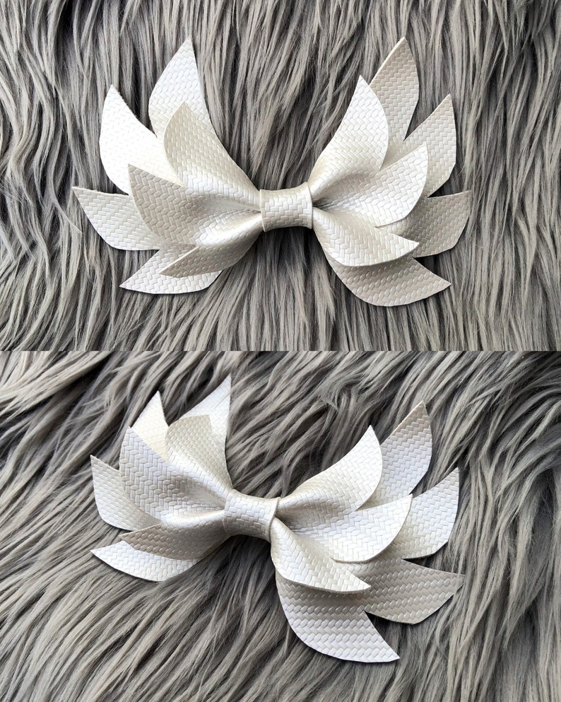 May include: A white faux leather bow with a layered, petal-like design. The bow is made of multiple pieces of leather that are sewn together to create a 3D effect.