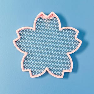 May include: A pink metal tray shaped like a flower with a white mesh design. The tray is ideal for holding small items such as jewellery or keys.
