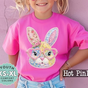 May include: Hot pink youth t-shirt with a colorful bunny graphic wearing heart-shaped glasses. The bunny has floral and patterned details. The shirt is available in sizes XS-XL.