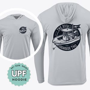 May include: A light gray UPF hoodie with long sleeves. The front features a small circular logo, while the back displays a larger graphic of a boat with the text "THE DOGHOUSE TWO." The hoodie is labeled as a 50+ sun shirt.