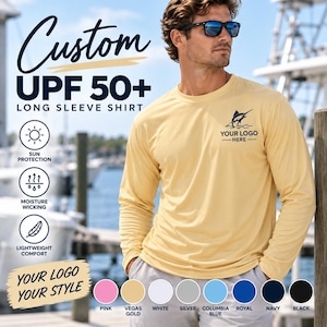 May include: A light yellow long-sleeve shirt with UPF 50+ sun protection, moisture-wicking, and lightweight comfort features. The shirt displays a marlin graphic and the text YOUR LOGO HERE on the chest, with color options including pink, vegas gold, white, silver, columbia blue, royal, navy, and black.