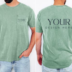 May include: A sage green t-shirt with a pocket on the front and the text "YOUR DESIGN HERE" printed on the pocket and back. The shirt is short-sleeved and has a relaxed fit. The model is wearing blue jeans.