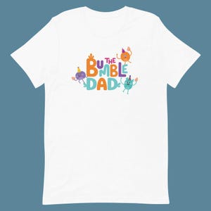Puede incluir: Camiseta blanca con el texto "BUMBLE DAD" en letras coloridas y personajes de dibujos animados. El dise&ntilde;o presenta figuras naranjas, moradas y turquesas con sombreros de fiesta, a&ntilde;adiendo un toque l&uacute;dico.