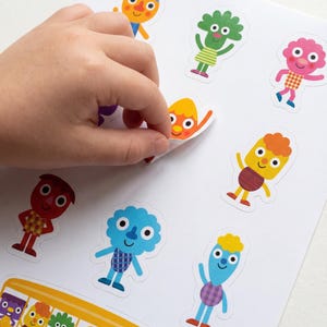 以下が含まれることがあります： カラフルな漫画のキャラクターのステッカーシート。ステッカーには、オレンジ、青、ピンクなどの明るい色で、さまざまなフレンドリーな外観のフィギュアが描かれています。手はステッカーの1つを剥がしています。笑顔の顔の黄色いスクールバスも表示されています。