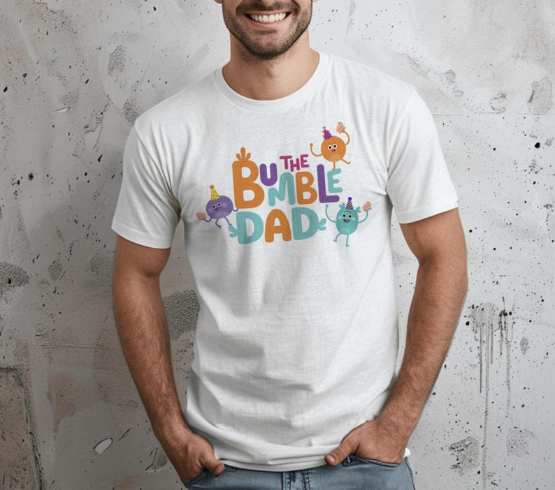 Puede incluir: Camiseta blanca con el texto "The Bumble Dad" en naranja, azul y verde. El dise&ntilde;o incluye personajes de dibujos animados con sombreros de fiesta. La camiseta es de cuello redondo y tiene mangas cortas.