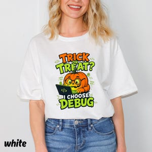 Könnte beinhalten: Ein weißes T-Shirt mit einer Grafik eines orangefarbenen Kürbisses, der eine Brille trägt und einen Laptop benutzt. Der Text lautet TRICK OR TREAT? I CHOOSE DEBUG, ergänzt durch kleine Geistersymbole und Code-Klammern.
