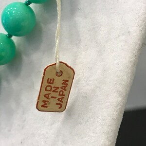 May include: Close-up of a turquoise beaded necklace with a tag that reads "MADE IN JAPAN". The necklace features large, round beads. The tag is rectangular with rounded corners and a string attached.