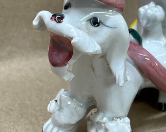 Op de afbeelding: Een witte keramische poedelfiguur met roze accenten op de hoed en mond. De poedel heeft zwarte ogen en staat in een speelse houding. Het beeldje maakt deel uit van een decoratief set.