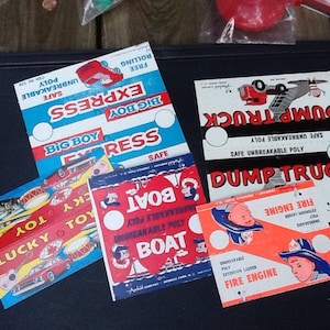 May include: A collection of vintage toy labels featuring colorful illustrations. The labels showcase various toy themes, including a fire engine, dump truck, boat, and race car. The labels are printed with the words "SAFE UNBREAKABLE POLY".