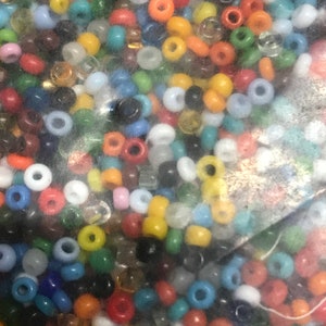 May include: A collection of small, colorful beads in various shades including red, orange, yellow, green, blue, and white. The beads are round with a hole through the center, suitable for jewelry making or crafts.