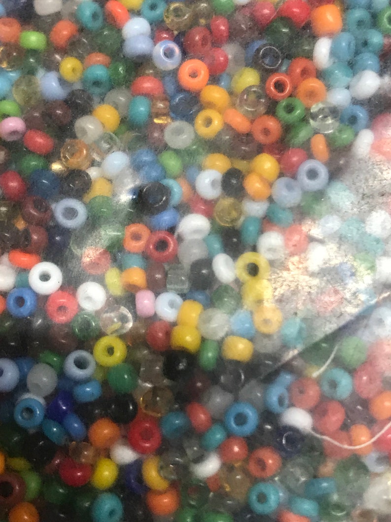 May include: A collection of small, colorful beads in various shades including red, orange, yellow, green, blue, and white. The beads are round with a hole through the center, suitable for jewelry making or crafts.