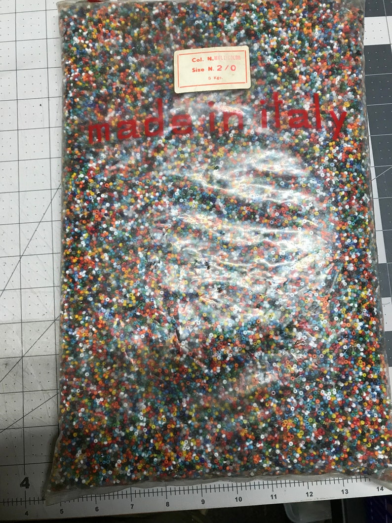 May include: A clear plastic bag filled with small, colorful beads. The beads are a mix of colors including red, orange, yellow, blue, and white. The bag has a label that reads "Col. N. Multicolor" and "Size N. 2/0". The text "made in italy" is visible.