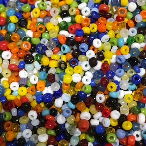 May include: A close-up shot of a collection of small, colorful glass beads. The beads are a mix of opaque and translucent, in a variety of colors including red, orange, yellow, green, blue, white, and black. The beads are round with a hole through the center.