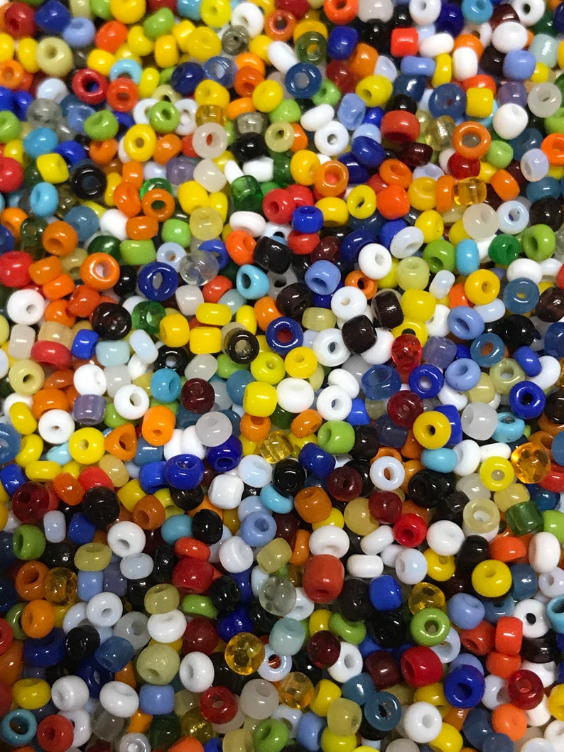 May include: A close-up shot of a collection of small, colorful glass beads. The beads are a mix of opaque and translucent, in a variety of colors including red, orange, yellow, green, blue, white, and black. The beads are round with a hole through the center.