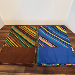 May include: Two rectangular scarves with diagonal stripes in the image. One scarf has brown, orange, yellow, and green stripes with a brown bottom. The other has blue, purple, pink, and yellow stripes with a blue bottom.