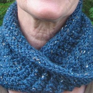 May include: A blue knitted infinity scarf with a speckled pattern. The scarf is folded in half and worn around the neck.