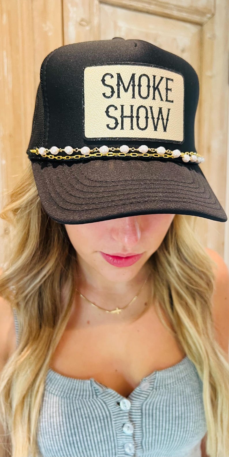 Puede incluir: Gorra de camionero negra con el texto "SMOKE SHOW" en un parche beige. La gorra presenta un detalle de cadena de perlas y oro en el borde. Un accesorio elegante para uso casual.