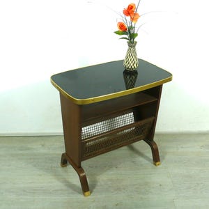 May include: A dark wood side table with a black glass top and a gold trim. The table has a shelf and a wire magazine rack.