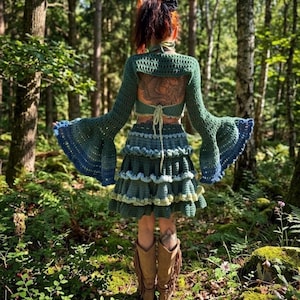 Può includere: Un completo in due pezzi all'uncinetto composto da un top bolero a maniche lunghe con ampie maniche a campana e una gonna a balze. Il set presenta tonalità verde bosco, salvia e blu, con chiusura a laccetti sul retro e motivo testurizzato.