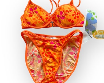May include: An orange bikini set with a floral pattern in shades of pink and orange. The top has adjustable straps and a clasp closure. The bottoms are a classic cut. A tag with a blue flower is attached.