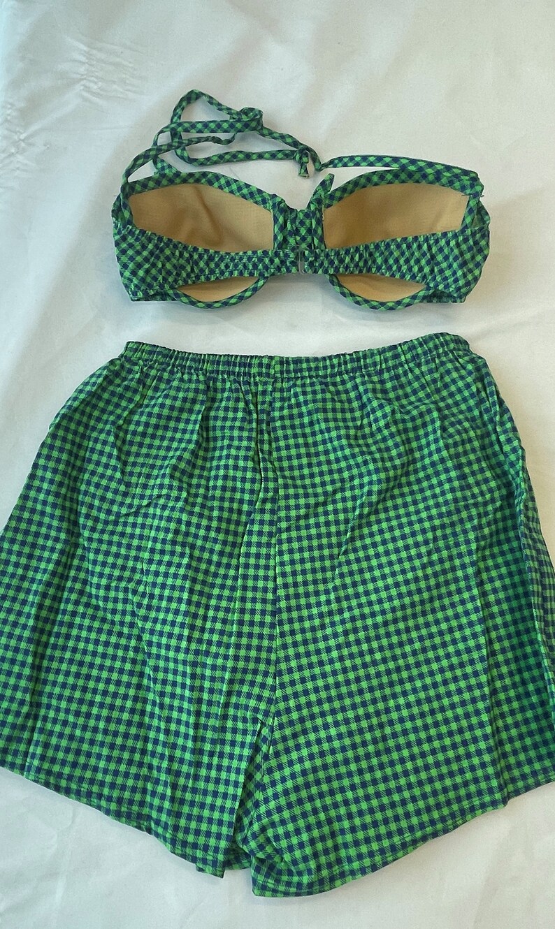 May include: A two-piece swimsuit set in a green and navy blue gingham pattern. The top is a halter-style bikini with a tie closure. The matching shorts have an elastic waistband. The swimsuit is made of a lightweight fabric.