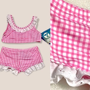 May include: Pink and white gingham swimsuit with white lace trim. The top has a scoop neck and the bottoms are shorts. The tag says "Kids Top".