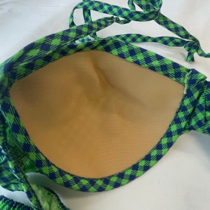 May include: A green and blue checkered bikini top with adjustable straps. The interior of the top is a light tan color. The bikini top is made of a soft, flexible material.