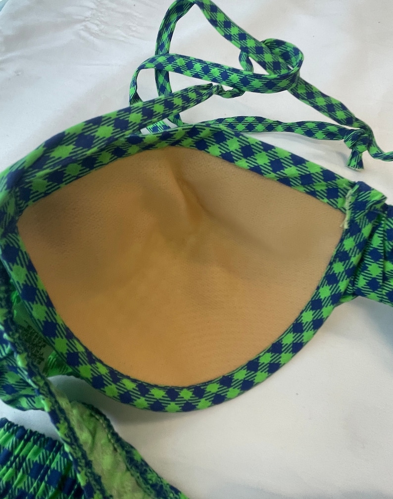 May include: A green and blue checkered bikini top with adjustable straps. The interior of the top is a light tan color. The bikini top is made of a soft, flexible material.