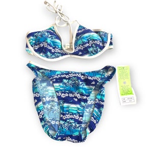 Puede incluir: Un traje de baño de dos piezas con estampado tropical. La parte superior e inferior del bikini presentan un estampado de palmeras y flores azules y blancas. La parte superior tiene cuello halter y ribete blanco. Una etiqueta está adjunta.