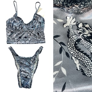May include: A two-piece swimsuit with a gray and white dragon print. The top is a cropped tank style with thin straps. The bottom is a high-cut bikini bottom.