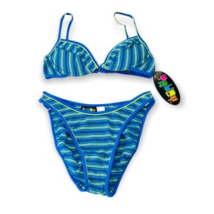Puede incluir: Un traje de baño de dos piezas con un estampado de rayas azules y verdes. El top del bikini tiene tirantes ajustables y un cierre de corchete. La parte inferior es de corte clásico. El traje de baño tiene ribetes azules y una etiqueta "COLOR".