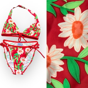 May include: Red bikini with a floral print of white daisies and green leaves. The bikini top is a halter style and the bottom is a tie-side style. The bikini is labeled "Bare Assets".