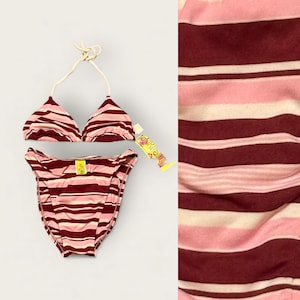 Puede incluir: Un conjunto de bikini de dos piezas con un estampado de rayas en tonos burdeos, rosa y blanco. La parte superior es de estilo triangular con tirantes halter, y la parte inferior es de corte clásico. Una etiqueta amarilla con texto adjunta.