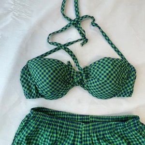 May include: A two-piece swimsuit set in a green and navy blue gingham pattern. The top is a halter style with a tie closure, and the bottoms are high-waisted with an elastic waistband. The fabric has a soft, textured appearance.