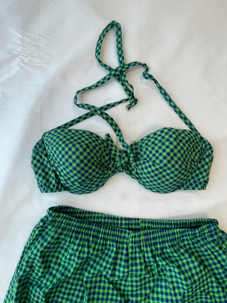 May include: A two-piece swimsuit set in a green and navy blue gingham pattern. The top is a halter style with a tie closure, and the bottoms are high-waisted with an elastic waistband. The fabric has a soft, textured appearance.