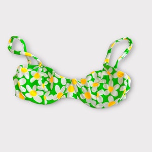 May include: A green bikini top with a white daisy print. The top has adjustable straps and a padded bra cup.