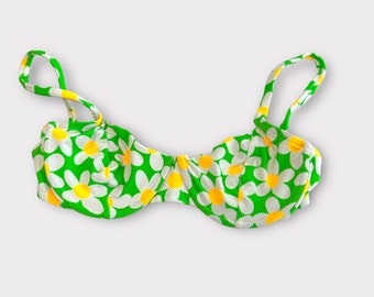 Könnte beinhalten: Ein grüner Bikini-Oberteil mit einem weißen Gänseblümchen-Druck. Das Oberteil hat verstellbare Träger und einen gepolsterten BH-Becher.