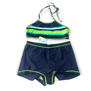 Puede incluir: Un conjunto de traje de baño de dos piezas. La parte superior halter es azul marino con rayas horizontales verdes, blancas y celeste. Los pantalones cortos a juego son azul marino con costuras verdes. Una etiqueta está adherida a los pantalones cortos.