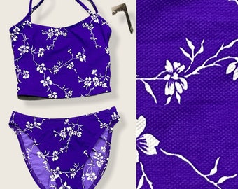 Può includere: Top e slip bikini con stampa floreale viola e bianca. La parte superiore ha spalline sottili e una scollatura rotonda. La parte inferiore è in stile a taglio alto.