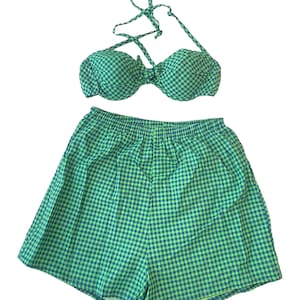 May include: A green and blue gingham two-piece swimsuit set. The set comprises a halter-neck bikini top and matching shorts with an elasticated waistband. The fabric has a classic, summery appearance.
