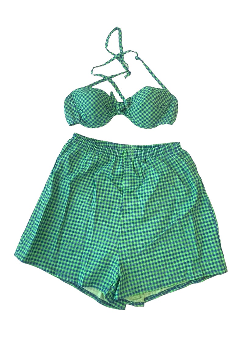 May include: A two-piece swimsuit set in a green and blue gingham pattern. The set includes a halter-style bikini top and matching shorts with an elastic waistband. The fabric has a classic, summery look.